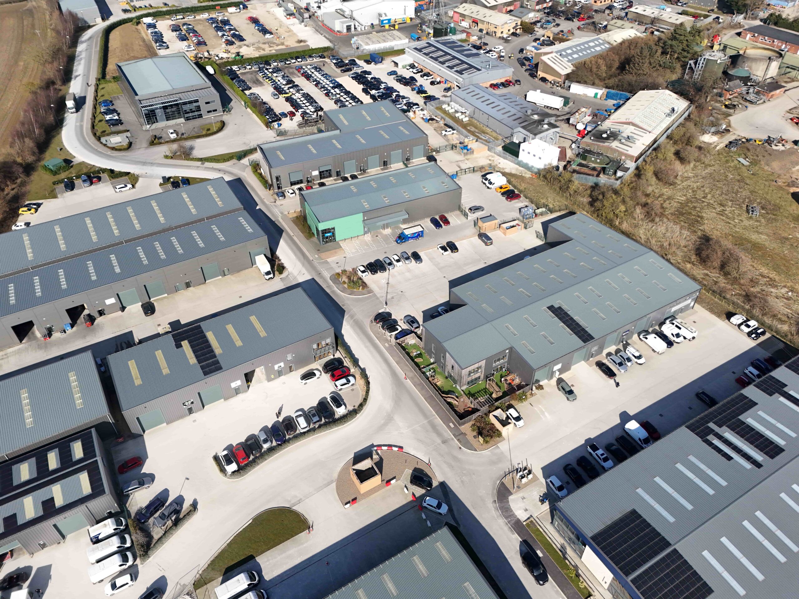 Aerial view of an industrial estate with multiple modern warehouse units, parking areas, and surrounding commercial buildings.