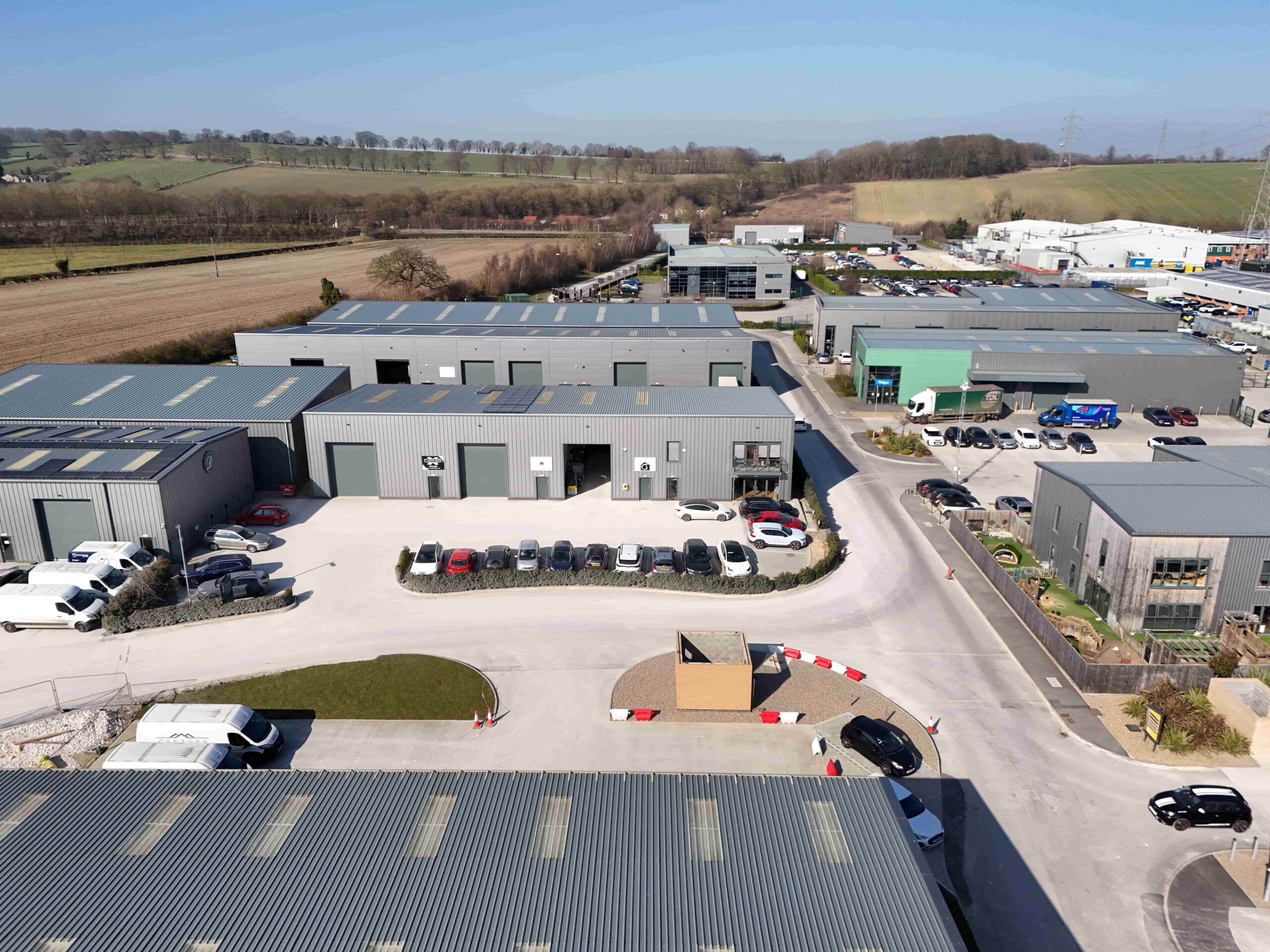 Photograph of industrial units with vehicles parked outside and countryside in the distance.