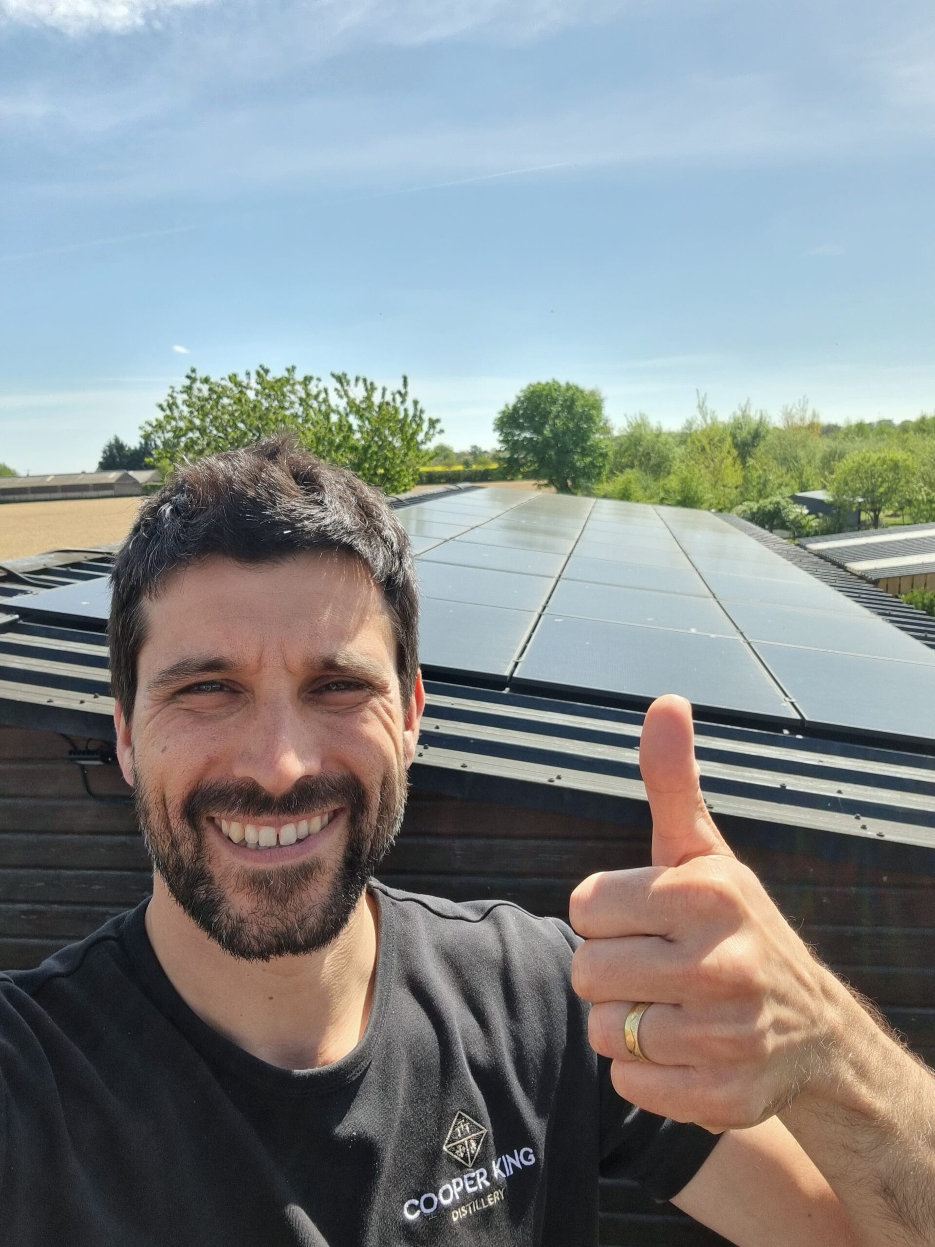 Person giving a thumbs-up in front of rooftop solar panels on a sunny day.
