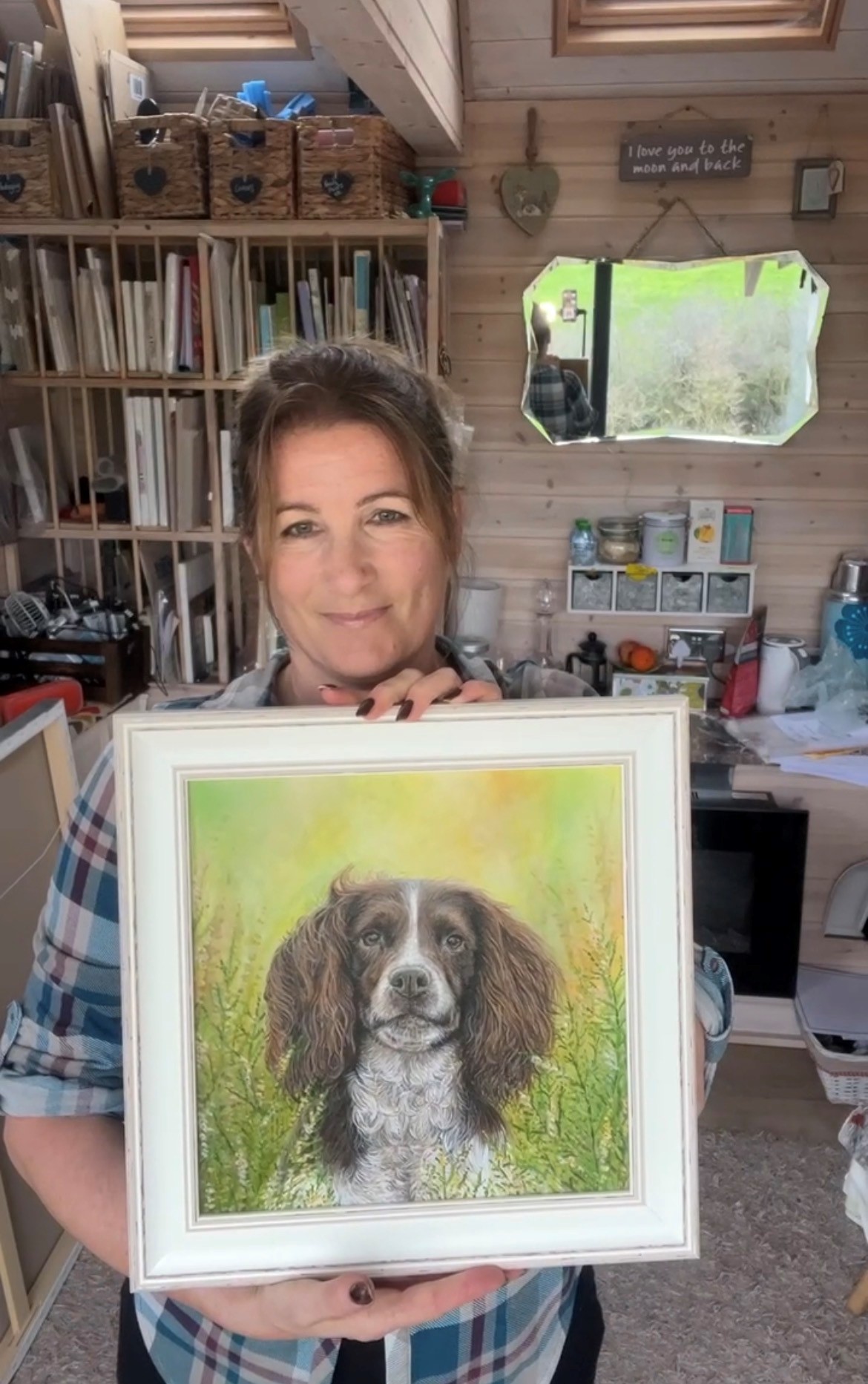 Person holding framed painting of a dog in an art studio