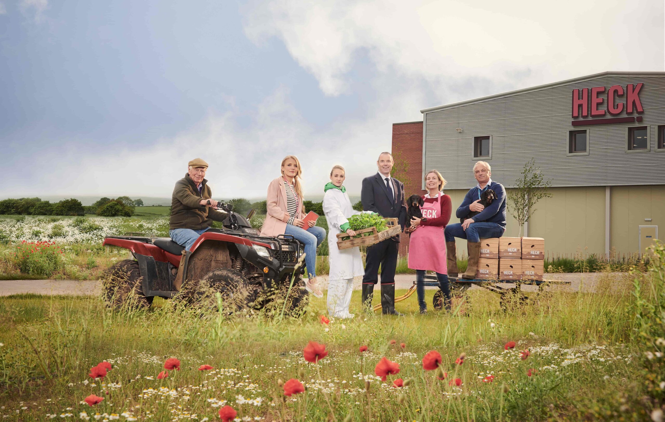People standing outside the HECK food production facility beside an ATV, crates of produce and wildflower meadow.