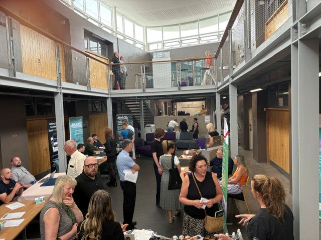 People attending a networking event inside the atrium of Springboard Business Centre, with attendees gathered around tables and seating areas on the ground floor and upper-level galleries overlooking the space.