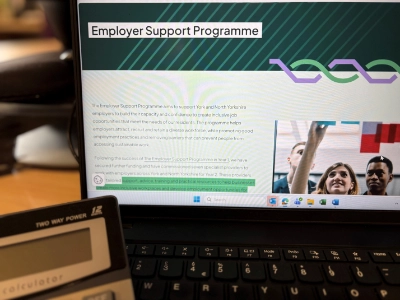 Laptop displaying information about an Employer Support Programme on a desk, with a calculator visible in the foreground.